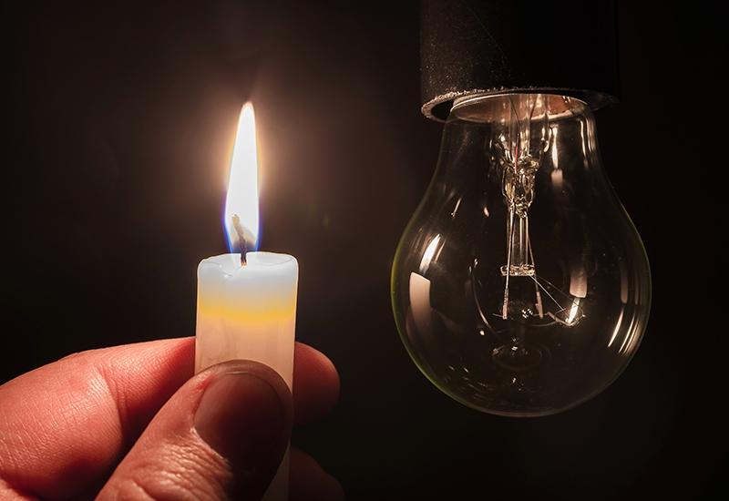 Article Cards Featured Image Burning candle near a switched off light bulb. Blackout, electri