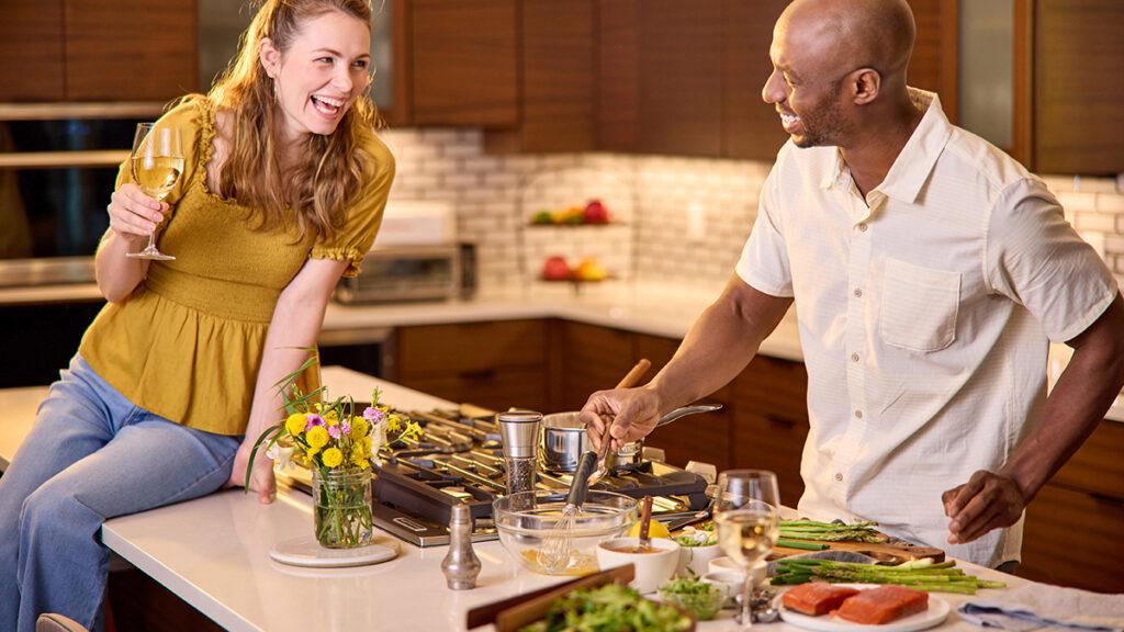 Couple cooking fish in a large kitchen and drinking wine.